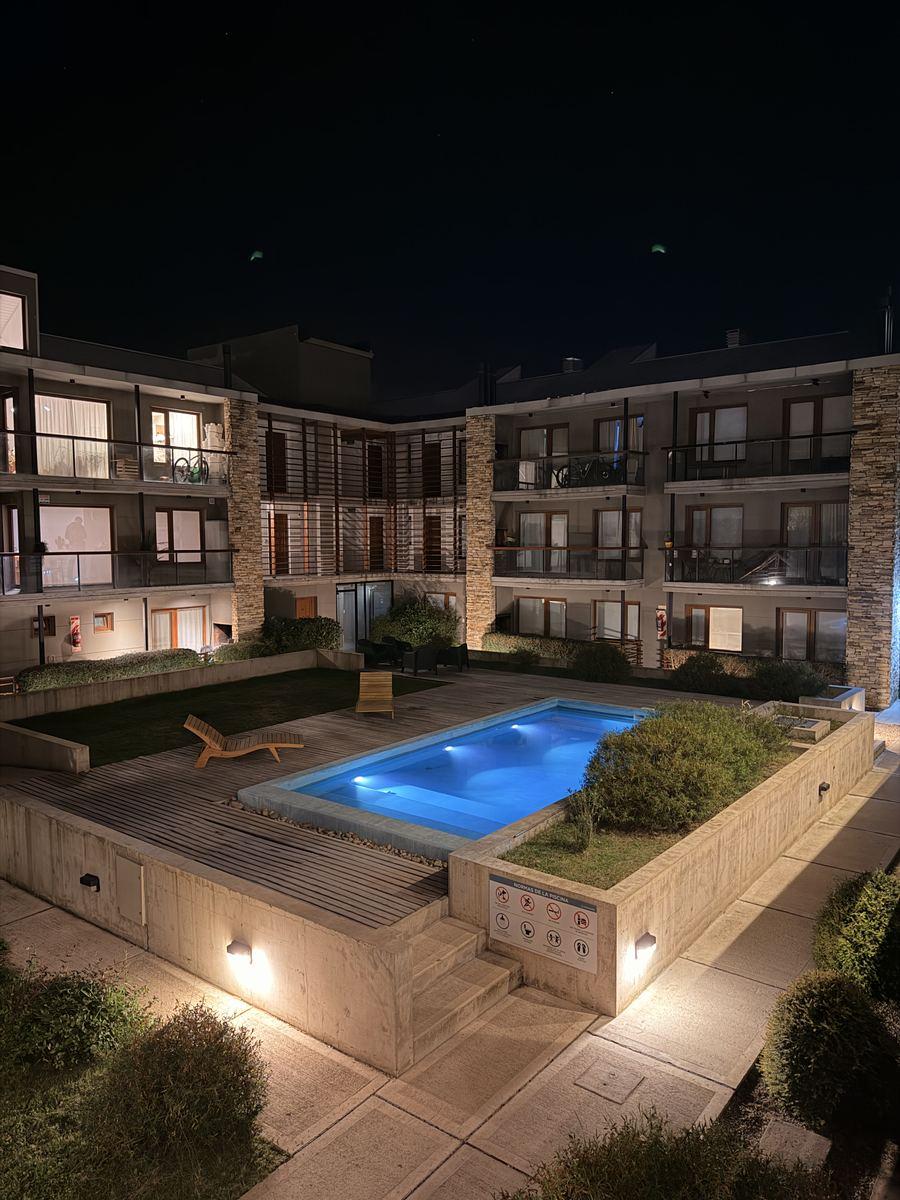 Piscina templada iluminada de noche en el patio del edificio Aliwen